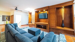 Una sala de estar moderna con un sofá seccional, un televisor de pantalla plana, paneles de madera y un ventilador de techo.