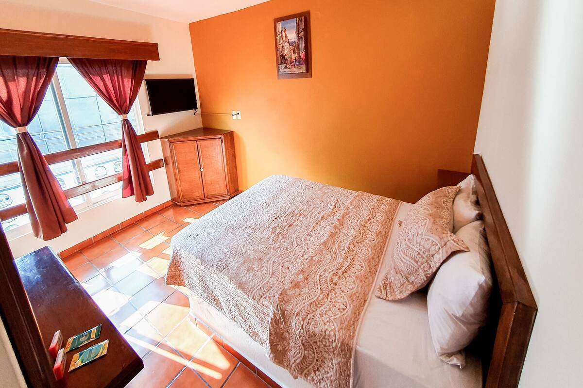 Ein Schlafzimmer mit einem Bett, Vorhängen, einem Fernseher, einem Gemälde und einem Holzschrank.