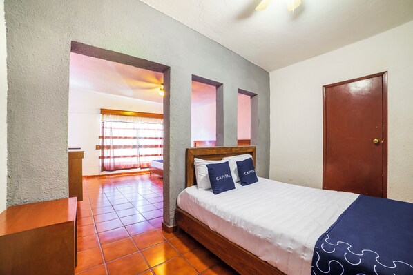 A hotel room with a wooden bed, a nightstand, a door, and a view of a balcony with curtains. - Capital O Hotel Casa Blanca (Celaya)