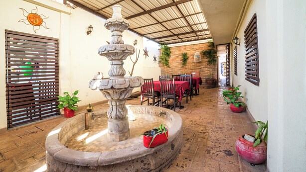 Un patio con una fuente de piedra, mesas a cuadros rojas y blancas, y plantas en macetas.