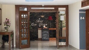 Entrada de hotel con puerta de madera, mostrador de recepción y un letrero que dice "Hotel Casa Blanca".