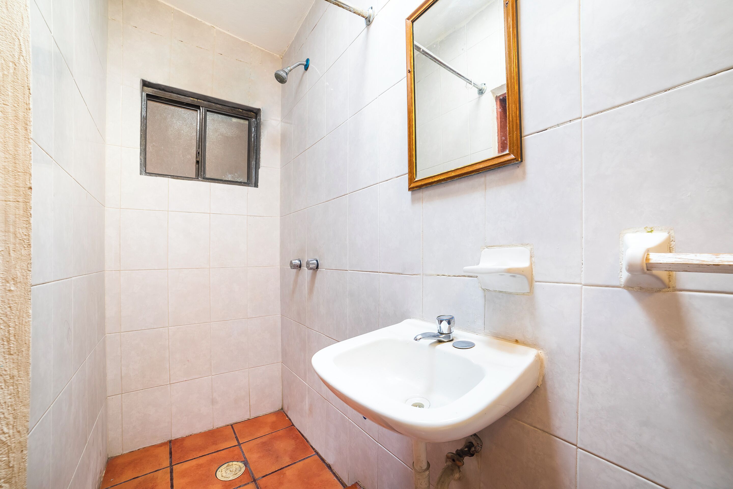A bathroom with white tiles, a white sink, a mirror, and a shower.