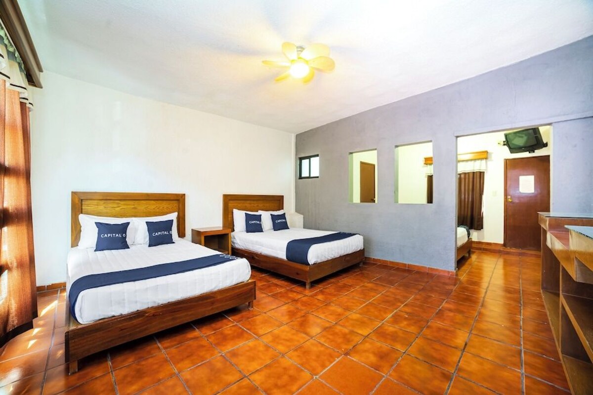 Habitación de hotel con dos camas, cabecera de madera, ventilador de techo y suelo de baldosas.