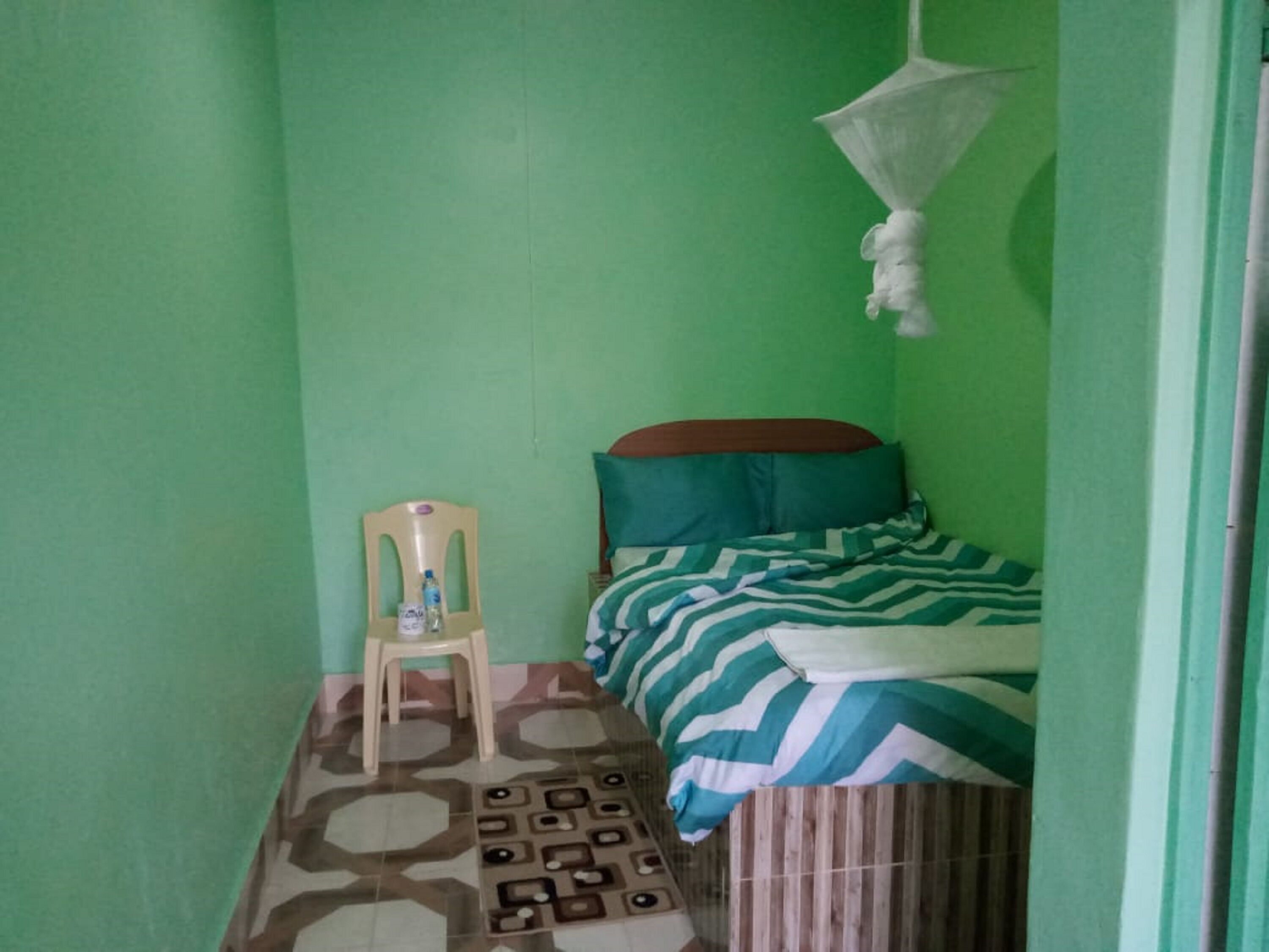 A small, green-walled room with a bed, a chair, and a mosquito net.