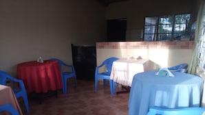 Un'area pranzo con sedie e tavoli di plastica blu, alcuni ricoperti da tovaglie bianche e rosse.