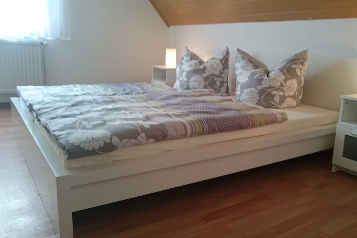 A bedroom with a bed, floral-patterned pillows, bedside tables, and a wooden floor.
