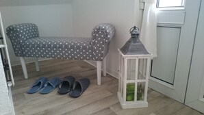 Ein kleiner Raum mit einem punktrasurigen Sofa, einem weißen Laternenlicht und einem Paar Hausschuhen auf dem Boden.