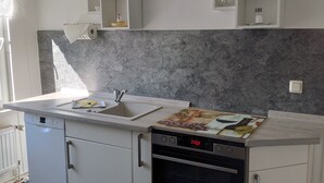 Eine moderne Küche mit Einbauofen, Spülmaschine und Spüle. Weiße Schränke und eine graue Spritzschutzwand sind vorhanden.