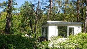 Eine kleine, weiße Hütte mit Veranda, umgeben von dichtem Wald.