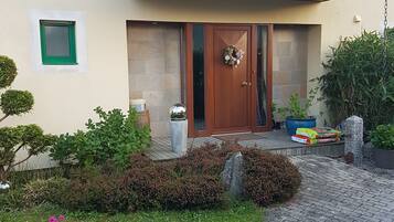 Una casa moderna con techo de tejas, una puerta principal con panel de vidrio y una ventana pequeña con marco verde.