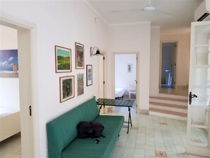 A room with a green sofa, a small table, and framed pictures on the wall.