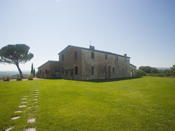 A large, two-story stone building with a flat roof, surrounded by a well-maintained lawn and a few trees.