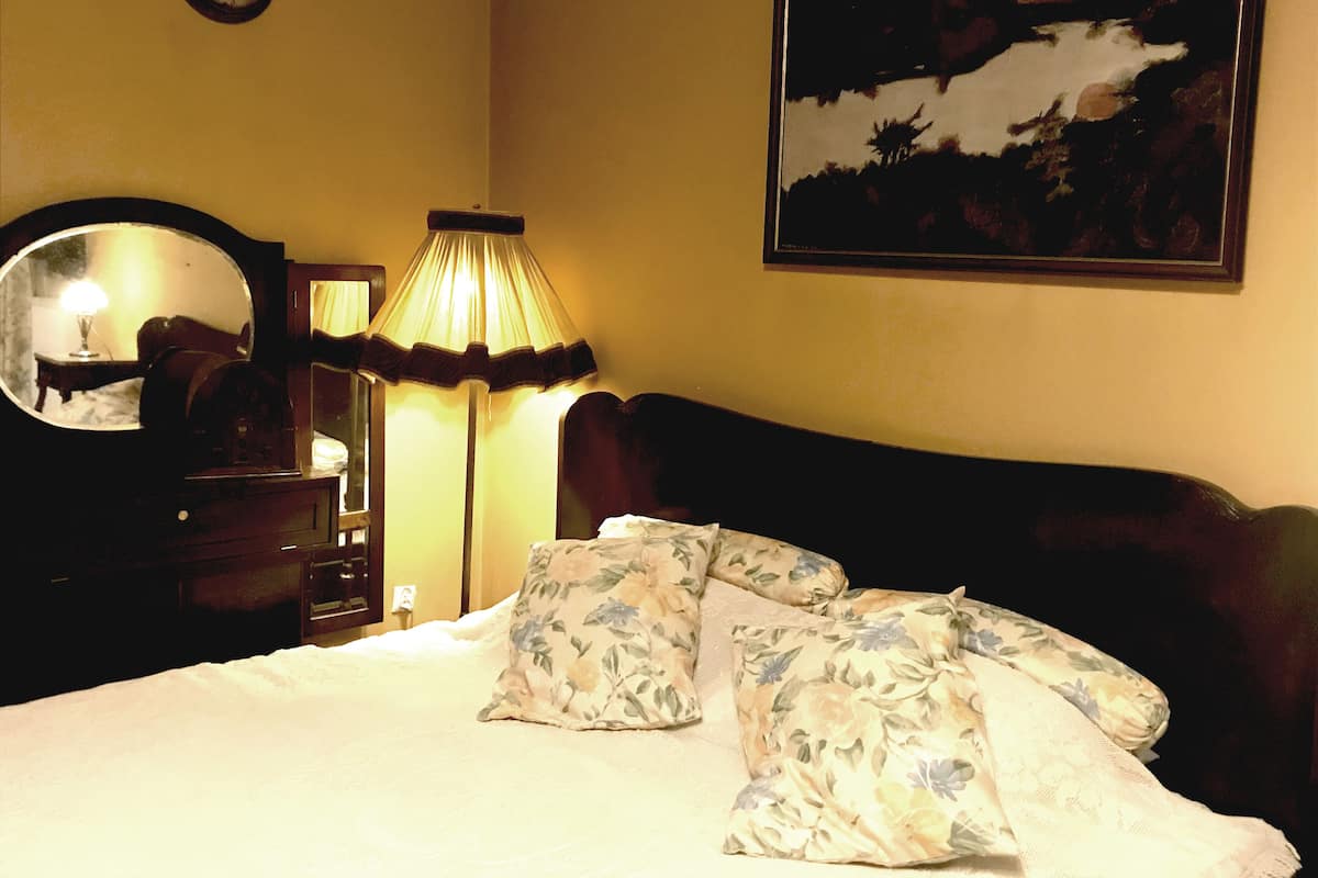 A bedroom with a bed, a lamp, a mirror, and a painting on the wall.