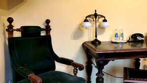 Una habitación con un sillón tapizado en verde, una mesa de madera con una lámpara y un teléfono.