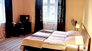 Habitación de hotel con cama, mesita de noche con lámpara, teléfono y ventana con cortinas.