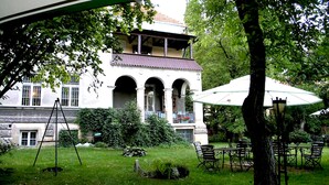 Un edificio blanco con un balcón, rodeado de vegetación y mobiliario exterior.