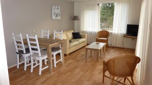 Un salon comprenant un canapé, une table à manger avec des chaises, une table basse, un téléviseur et une fenêtre avec des rideaux.