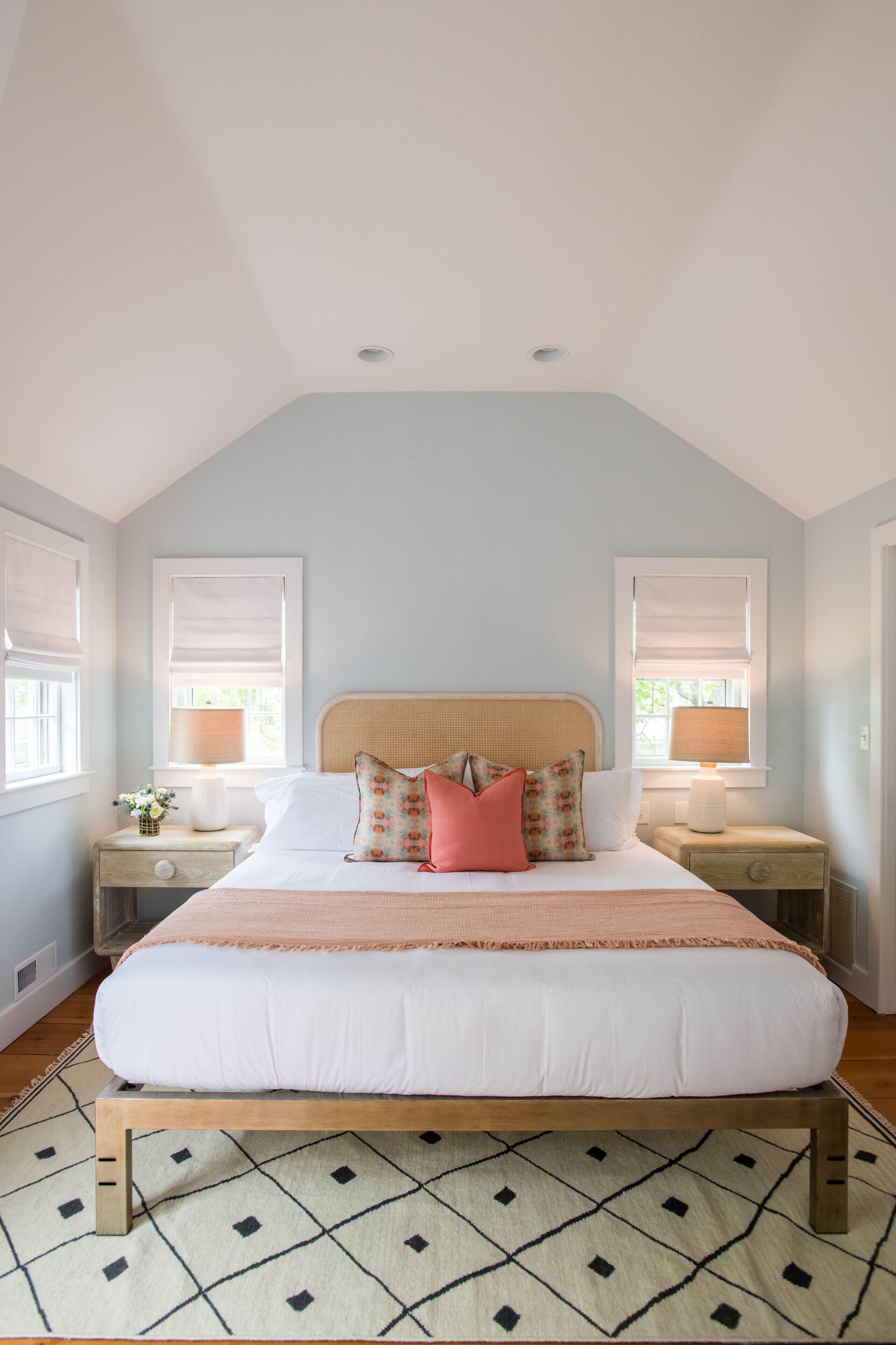 A bedroom with a large bed, two bedside tables, a window with a blind, and a patterned rug.