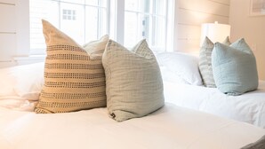 Ein ordentlich bezogenes Bett mit vielen Kissen und einer Lampe auf einem Nachttisch.