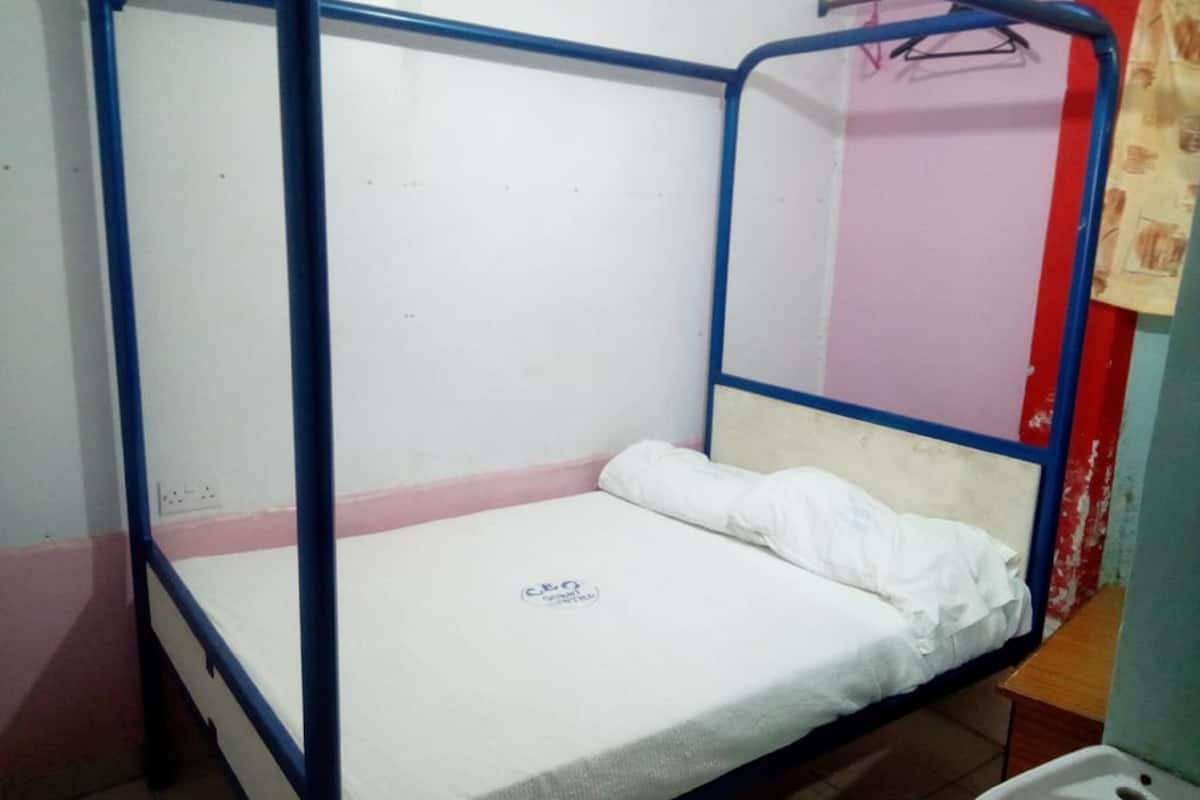 Un lit simple avec un cadre en métal bleu et un matelas blanc, dans une pièce aux murs roses et rouges.