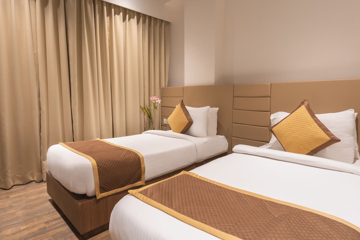 A hotel room with two beds, beige curtains, and a wooden floor.