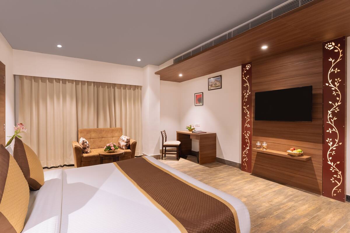 A hotel room with a large bed, a desk, a chair, a TV, and a small table with a fruit basket.