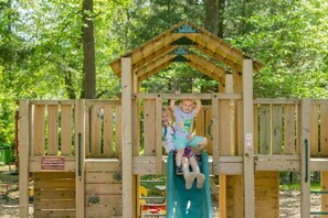 Una estructura de madera para jugar con un tobogán y un pequeño refugio con forma de casa.