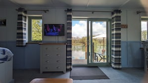 Una habitación con televisión, tocador de madera, ventana con cortinas y vista a un lago.