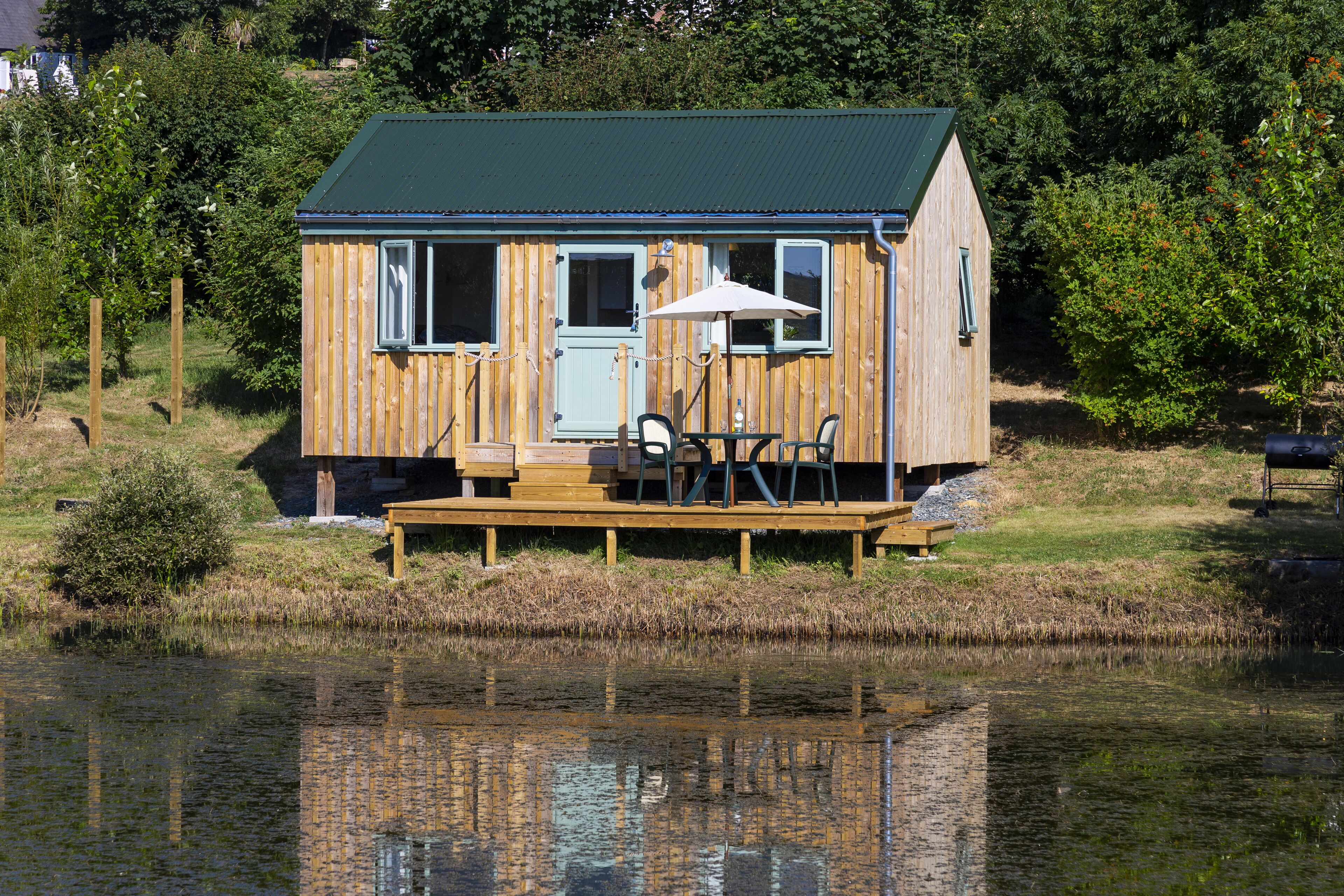 A wooden cabin with a green roof, a deck, and a table with chairs.