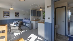 Una habitación luminosa con una cama, una pequeña cocina y un baño.