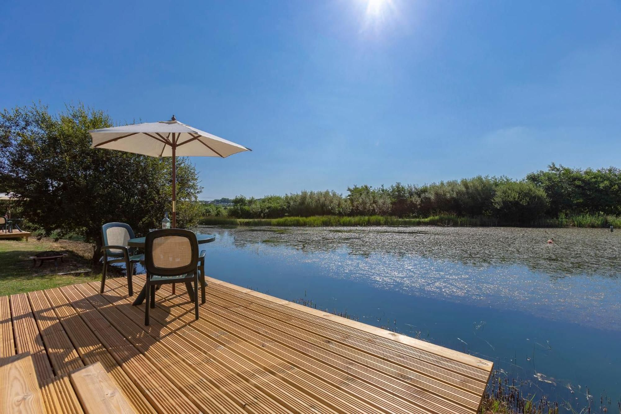A wooden deck with a table and chairs, an umbrella, and a view of a calm river.