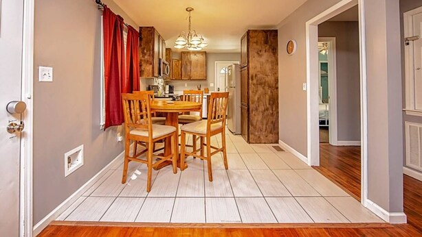 Un comedor con una mesa y sillas de madera, una araña y una cocina al fondo.
