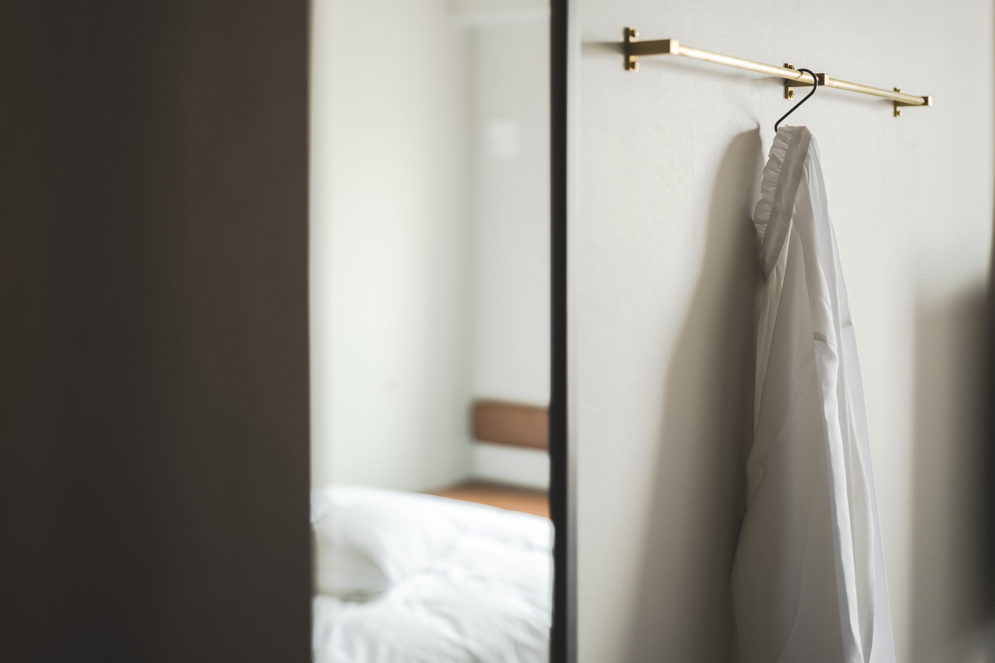 A room with a bed, a wooden headboard, and a hanging garment on a rod.