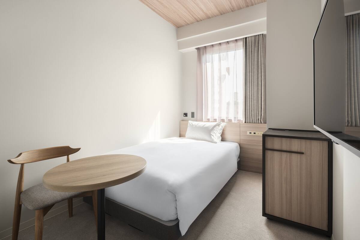 A hotel room with a bed, a desk, a chair, and a television.