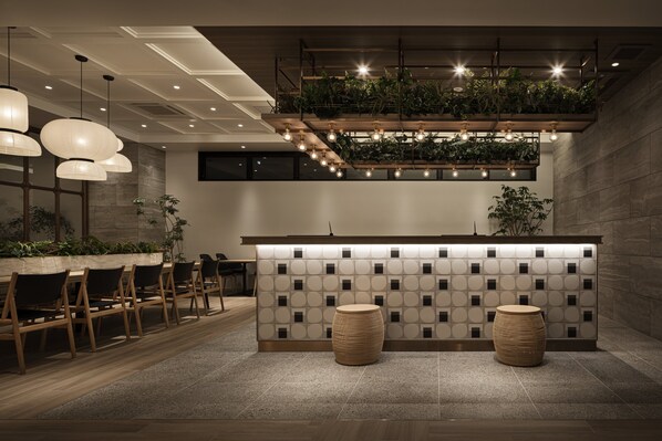 A modern reception area with a wooden reception desk, multiple seating arrangements, and a ceiling with hanging lights and greenery.