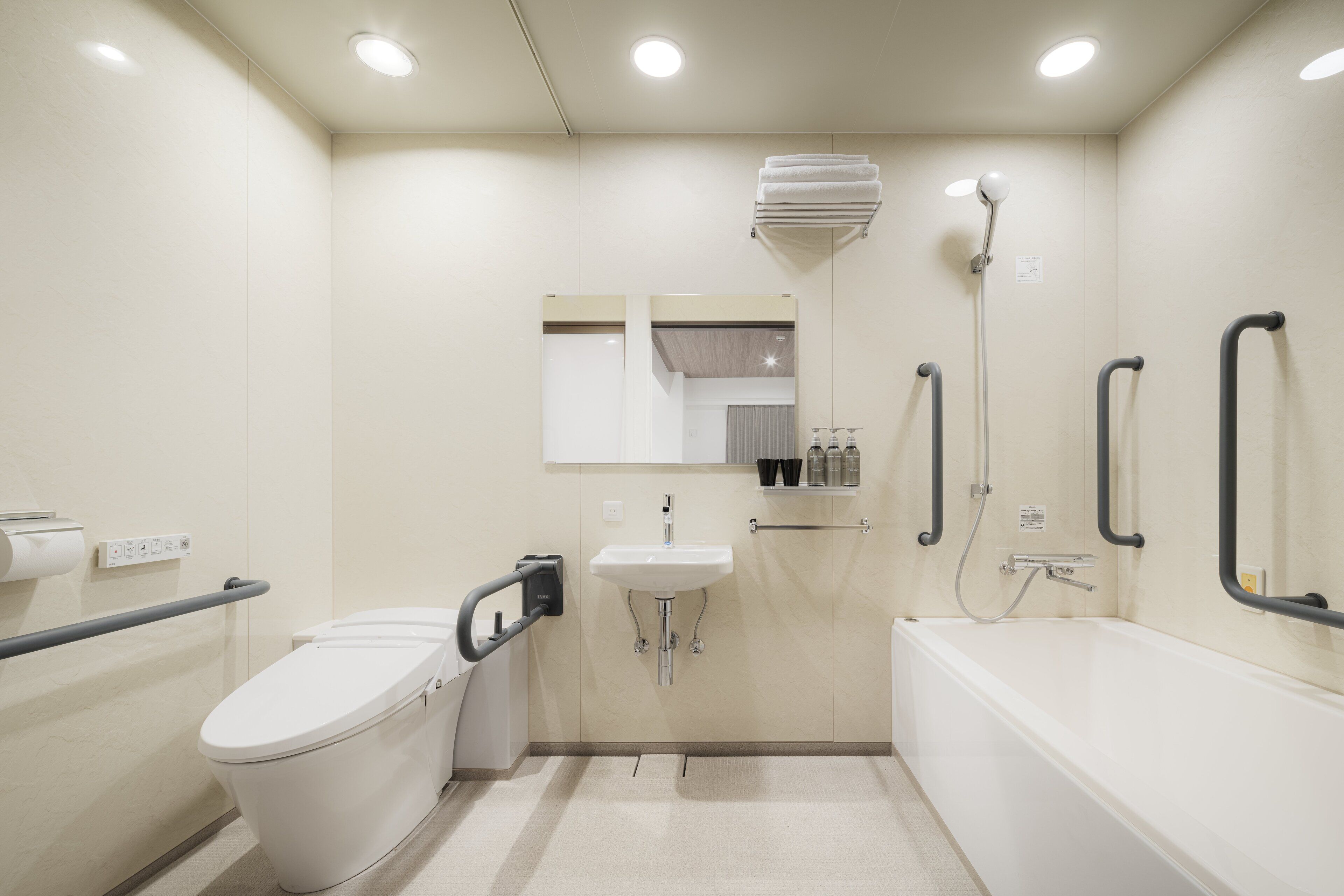 A small, modern bathroom with a toilet, sink, and bathtub. It includes grab bars and a showerhead.