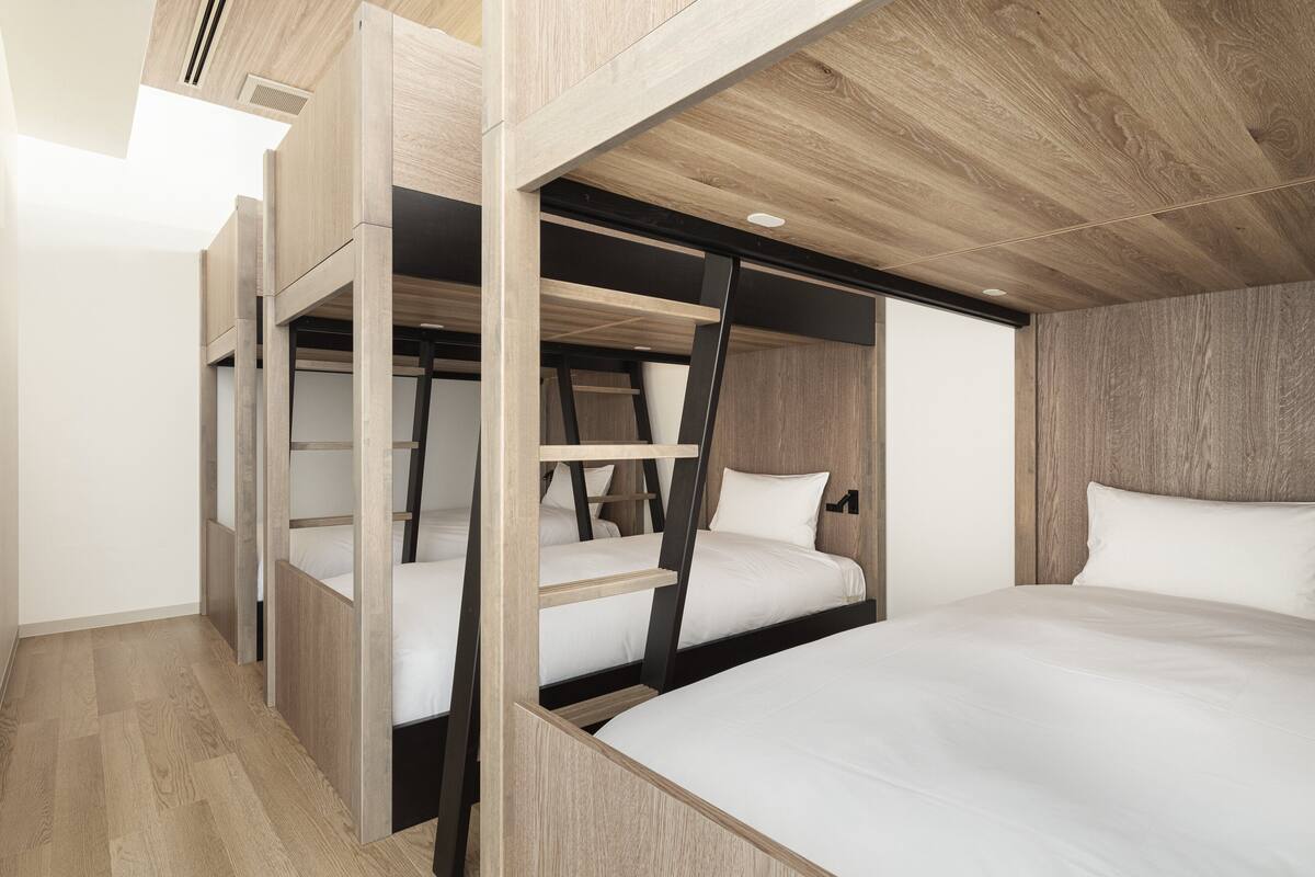 A modern hotel room with bunk beds, wooden flooring, and a sloped ceiling with recessed lighting.