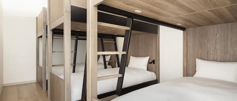 A modern hotel room with bunk beds, wooden flooring, and a sloped ceiling with recessed lighting.