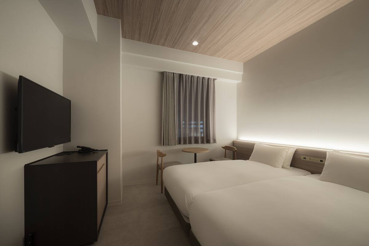 A modern hotel room with a large bed, a flat-screen TV, a small desk, and a window with curtains.
