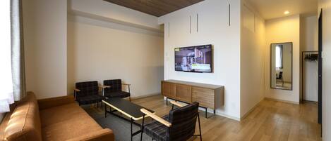 A modern living room with a sofa, chairs, a coffee table, a TV mounted on the wall, and a wooden cabinet.