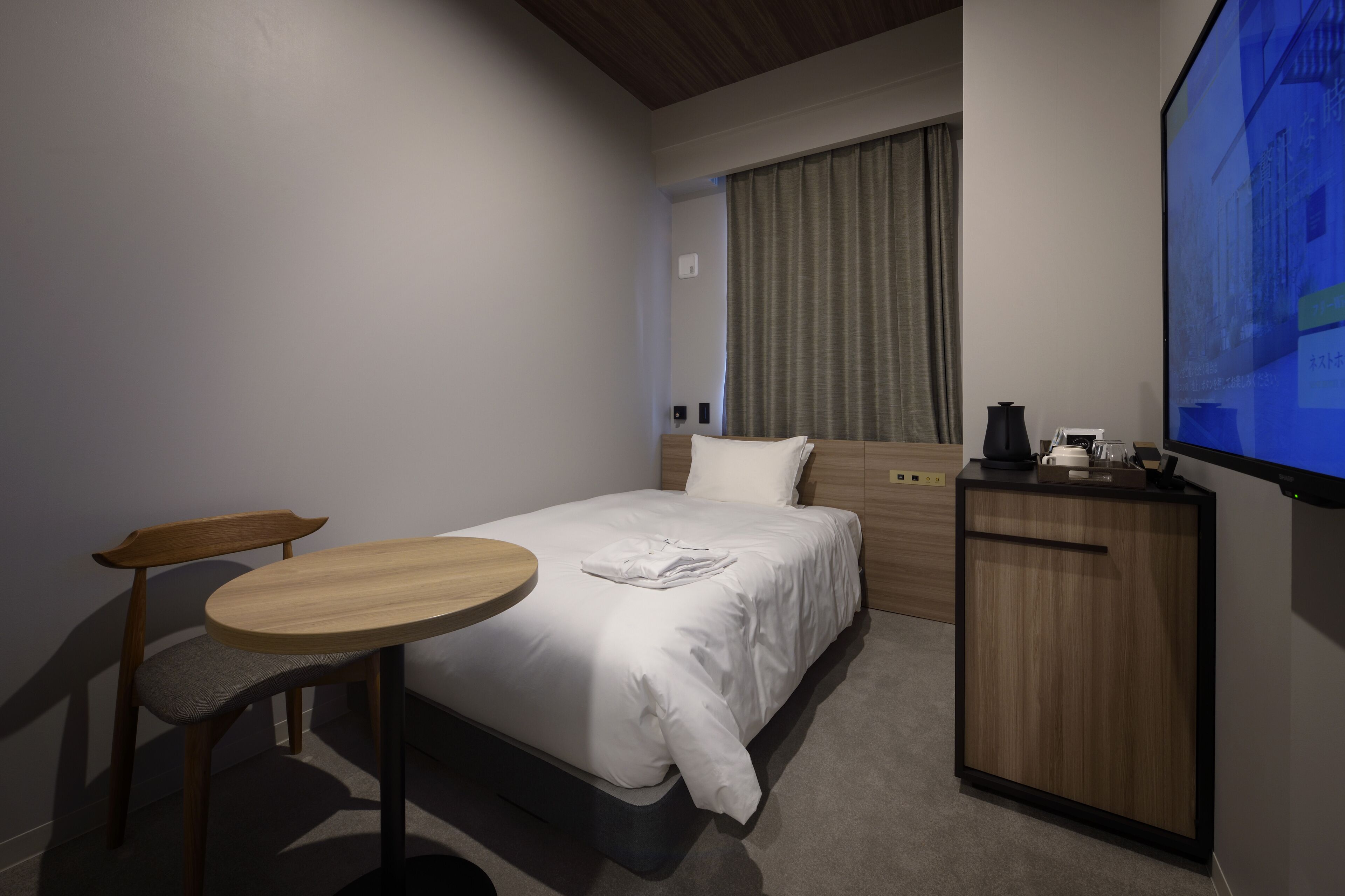 Une chambre d’hôtel avec un lit, un bureau, une chaise, une petite table et un téléviseur fixé au mur.