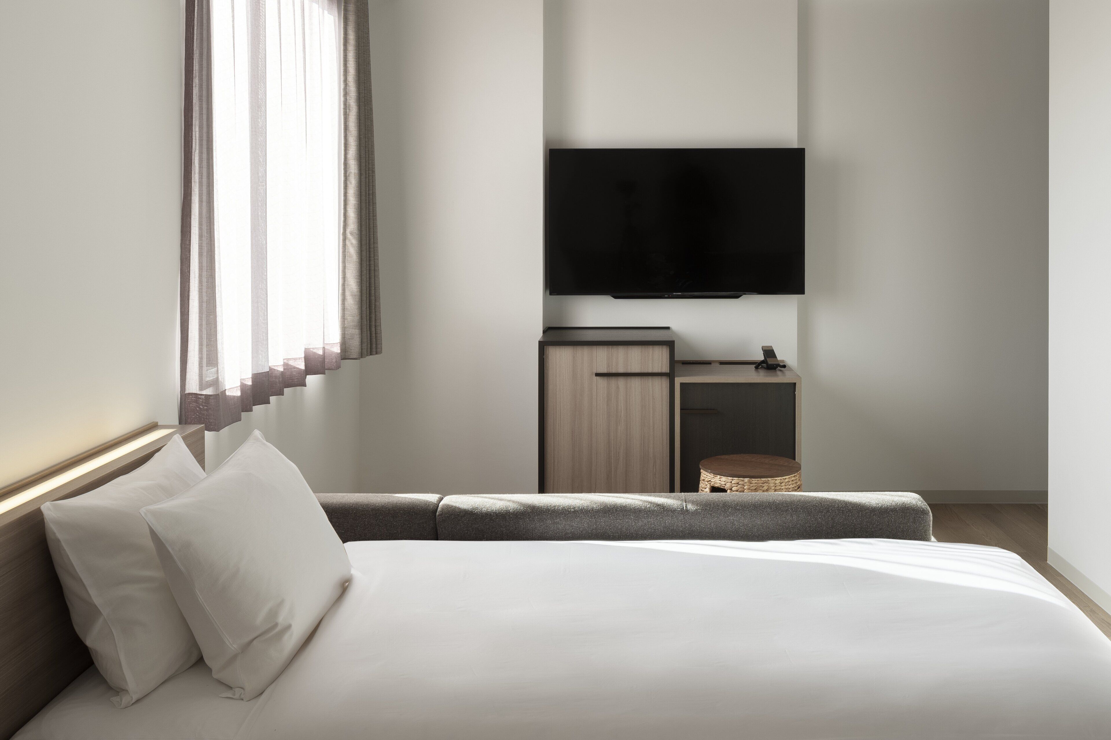 Ein modernes Hotelzimmer mit einem großen Bett, einem flachbildfernseher an der Wand, einer kleinen Holzkommode und einem Korbwäscher.