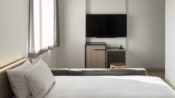 Ein modernes Hotelzimmer mit einem großen Bett, einem flachbildfernseher an der Wand, einer kleinen Holzkommode und einem Korbwäscher.