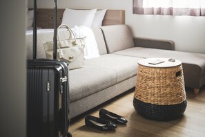Une chambre d’hôtel avec un lit, un canapé, un panier en osier, une valise et une paire de chaussures.