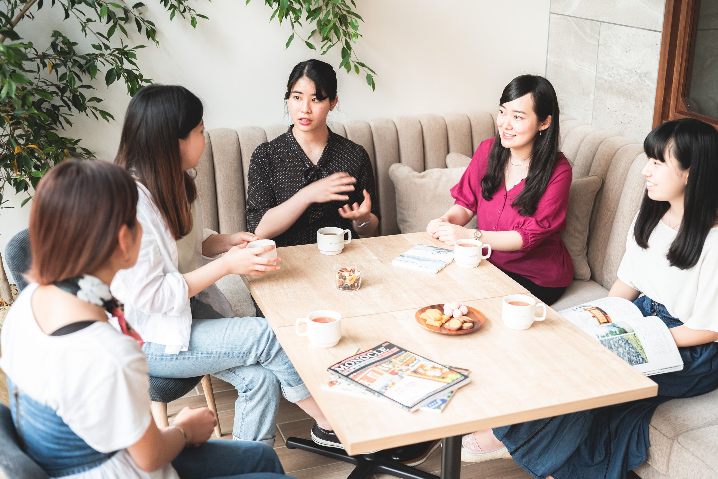 A group of people sitting around a table with coffee cups, a magazine, and a plate of cookies.