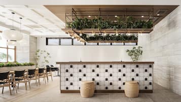 Un área de recepción moderna con un mostrador de madera, una pared adornada con plantas y una zona de estar con dos taburetes redondos.