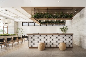 Un área de recepción moderna con un mostrador de madera, una pared adornada con plantas y una zona de estar con dos taburetes redondos.