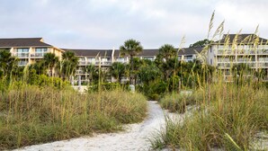 Un hôtel situé en bord de mer, doté de nombreux balcons et entouré de hautes herbes et de palmiers.