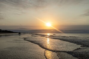 A beach with the sun setting over the horizon, waves gently lapping at the shore. - Ocean view condo with BEST location on the island!  (Hilton Head Island)