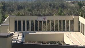 Vue sur la plage depuis un balcon, avec un panneau indiquant «
Il est interdit de fumer sur la promenade
».